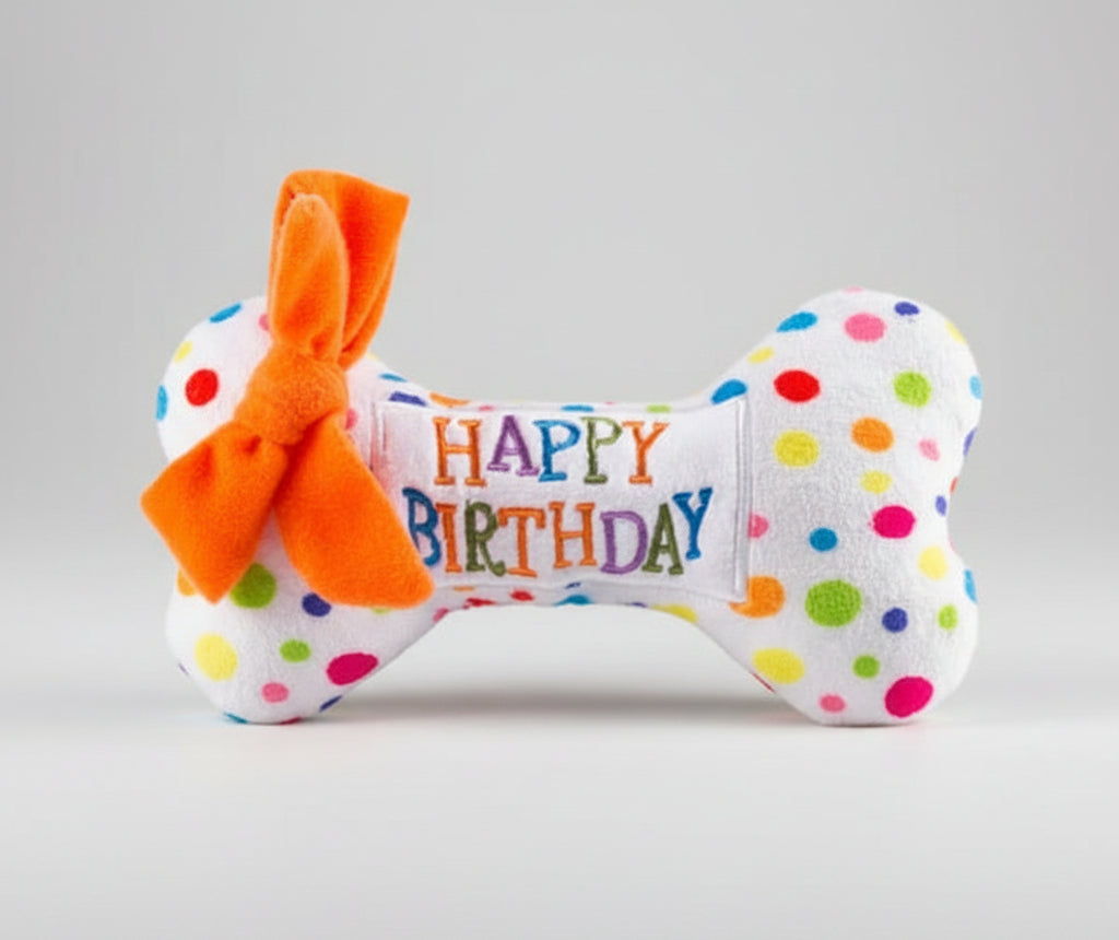 Plush birthday dog toy bone with orange bow and 'Happy Birthday' belly patch
