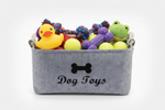 Light grey felt storage basket with bone logo and handles, filled with dog toys