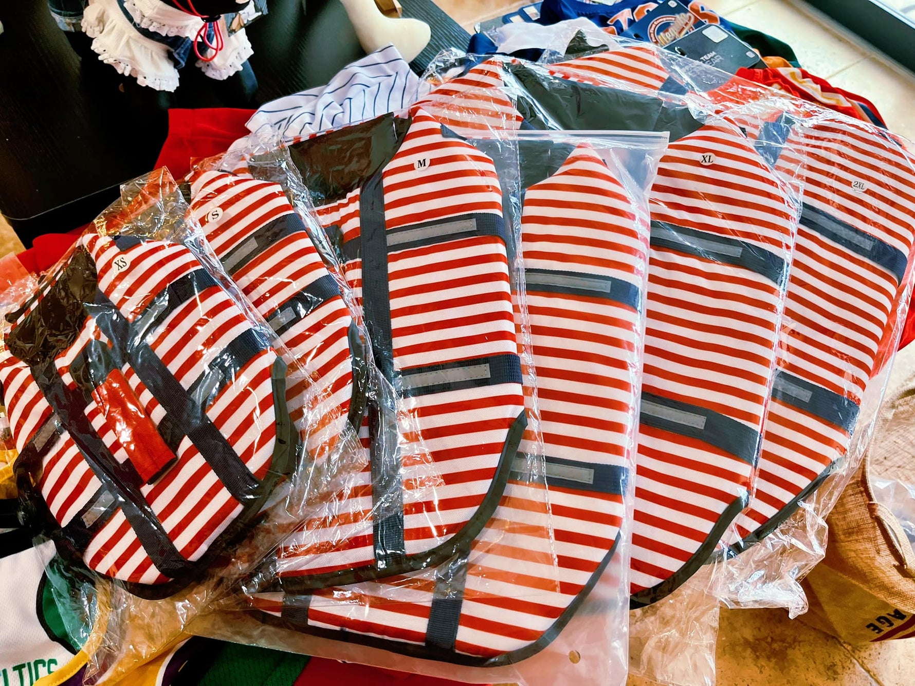 Pack of striped dog life jackets in plastic bags, red white navy with safety straps