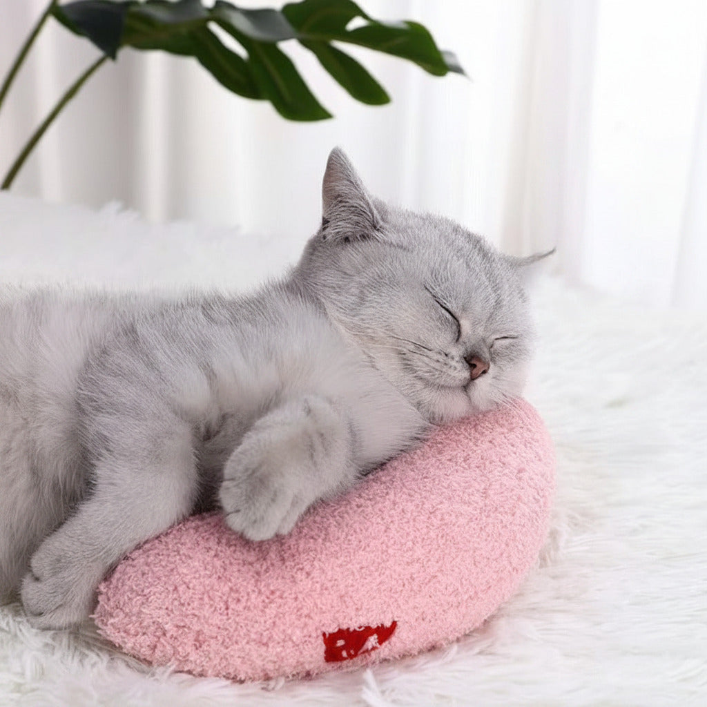Pink U-shaped plush cat pillow toy with small red patch, on a soft resting surface
