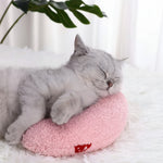 Pink U-shaped plush cat pillow toy with small red patch, on a soft resting surface
