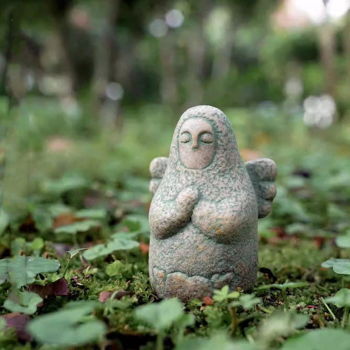 Speckled gray stone guardian ornament on moss, closed eyes, hands clasped