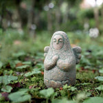 Speckled gray stone guardian ornament on moss, closed eyes, hands clasped