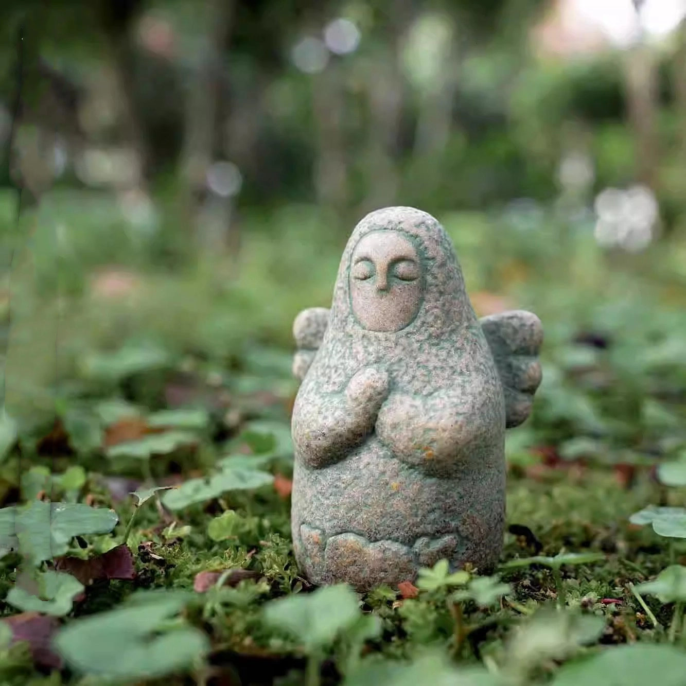 Speckled gray stone guardian ornament on moss, closed eyes, hands clasped