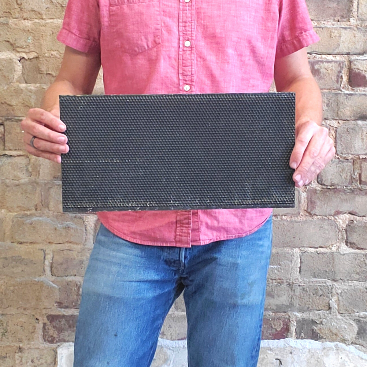 Rectangular dark plastic foundation sheet held in hands, hexagonal pattern