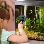 Small girl pointing at round digital fish tank thermometer showing 8.5°F