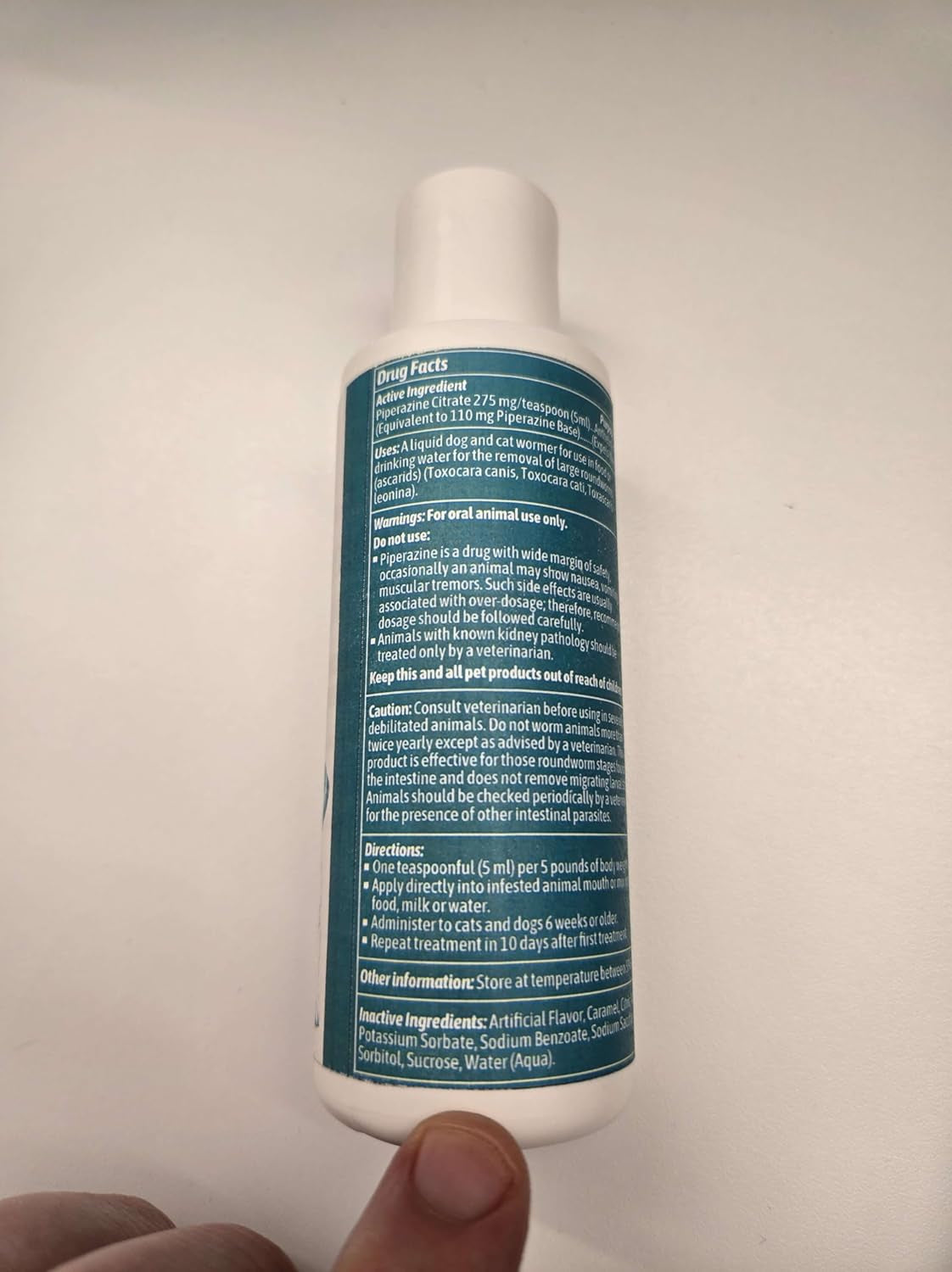 Liquid wormer bottle back view held in hand, white with teal label