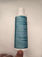 Liquid wormer bottle back view held in hand, white with teal label