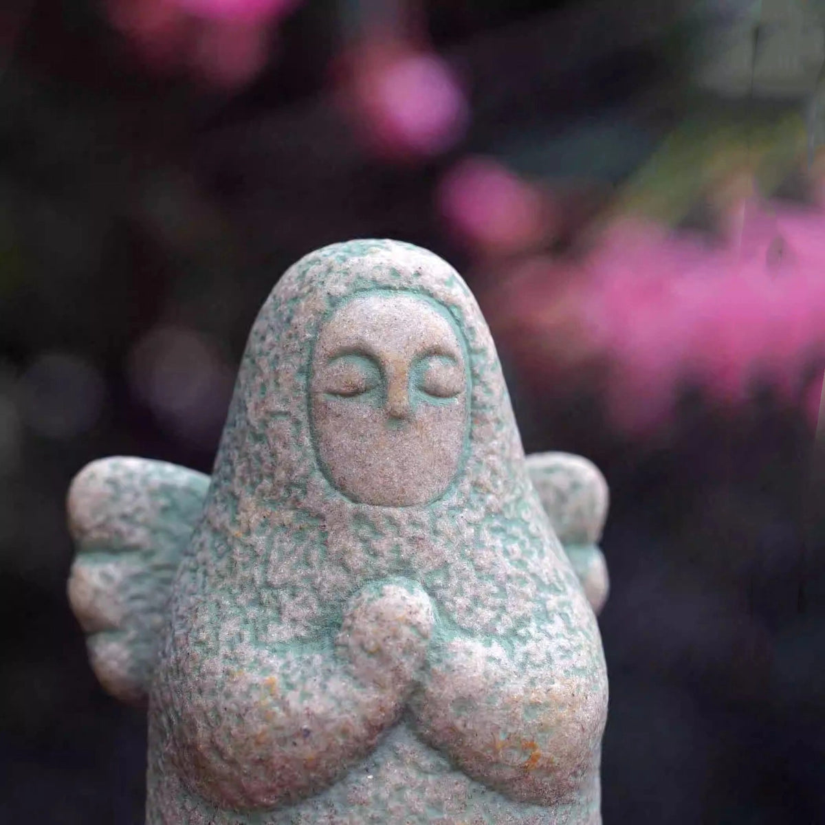 Close-up speckled gray stone guardian ornament with hood and clasped hands