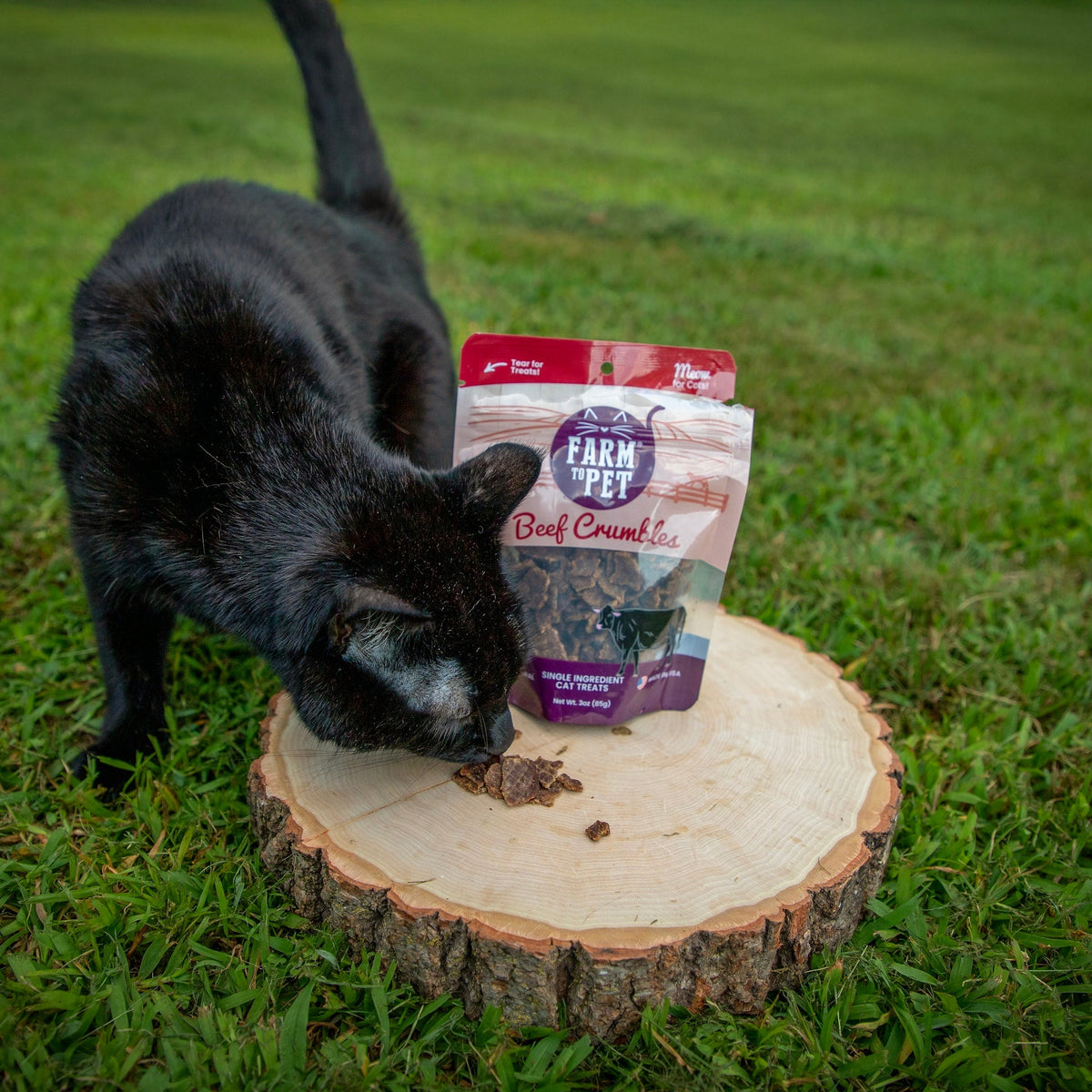 Beef Crumbles cat treat pouch beside a few crumbs on a wooden log slice