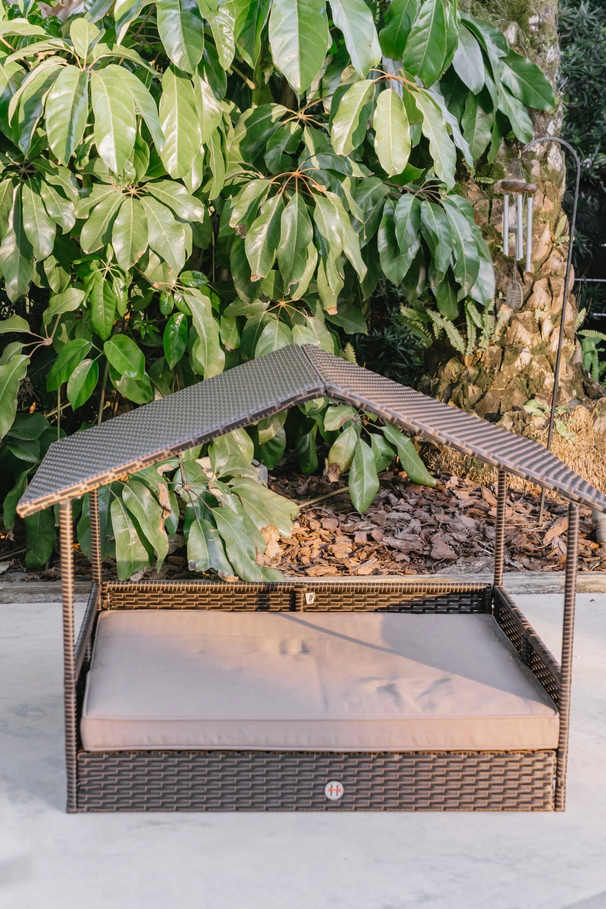 Outdoor raised pet cabana bed with dark wicker sides and beige cushion