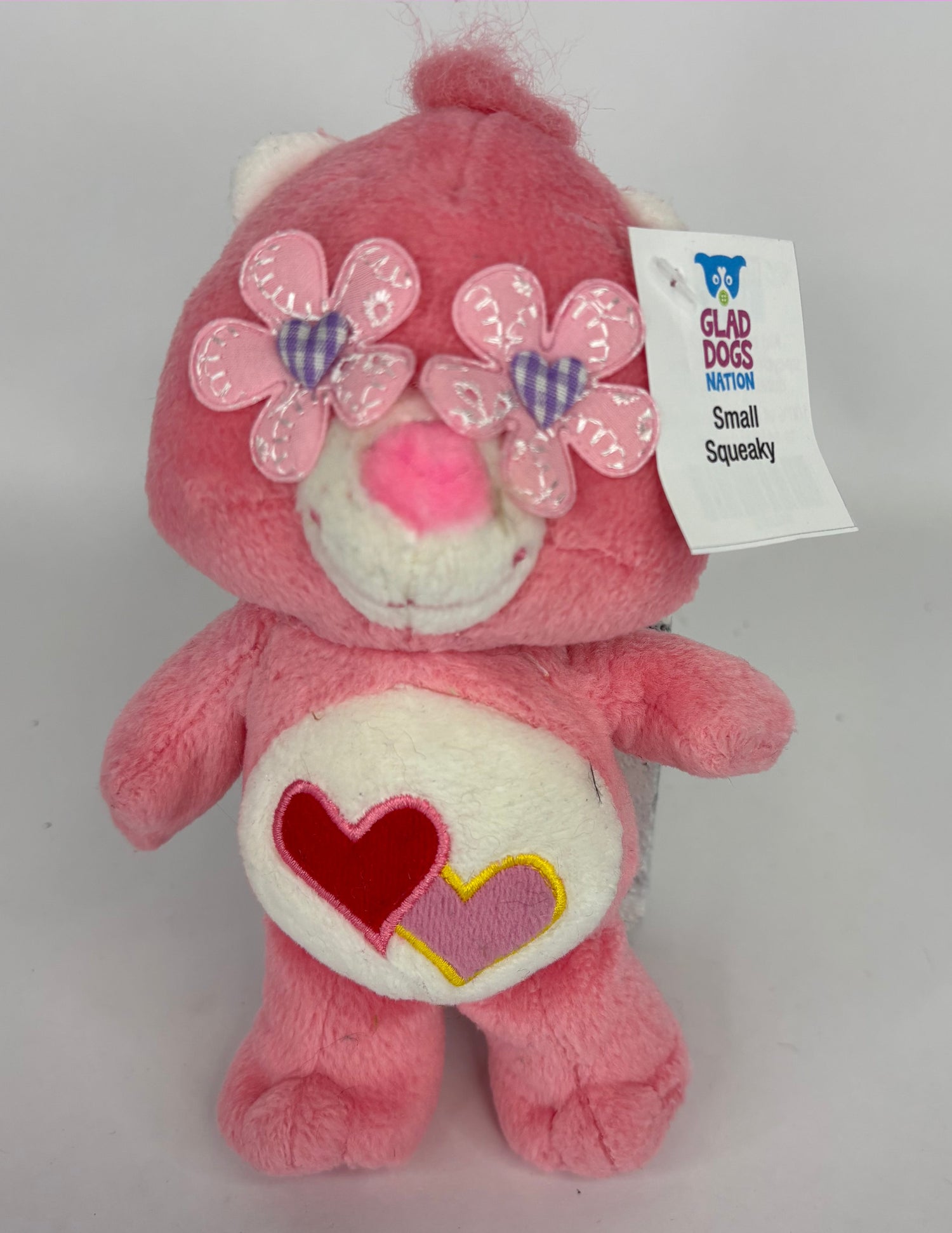 Pink plush dog toy bear with bow accents and heart-shaped belly applique.