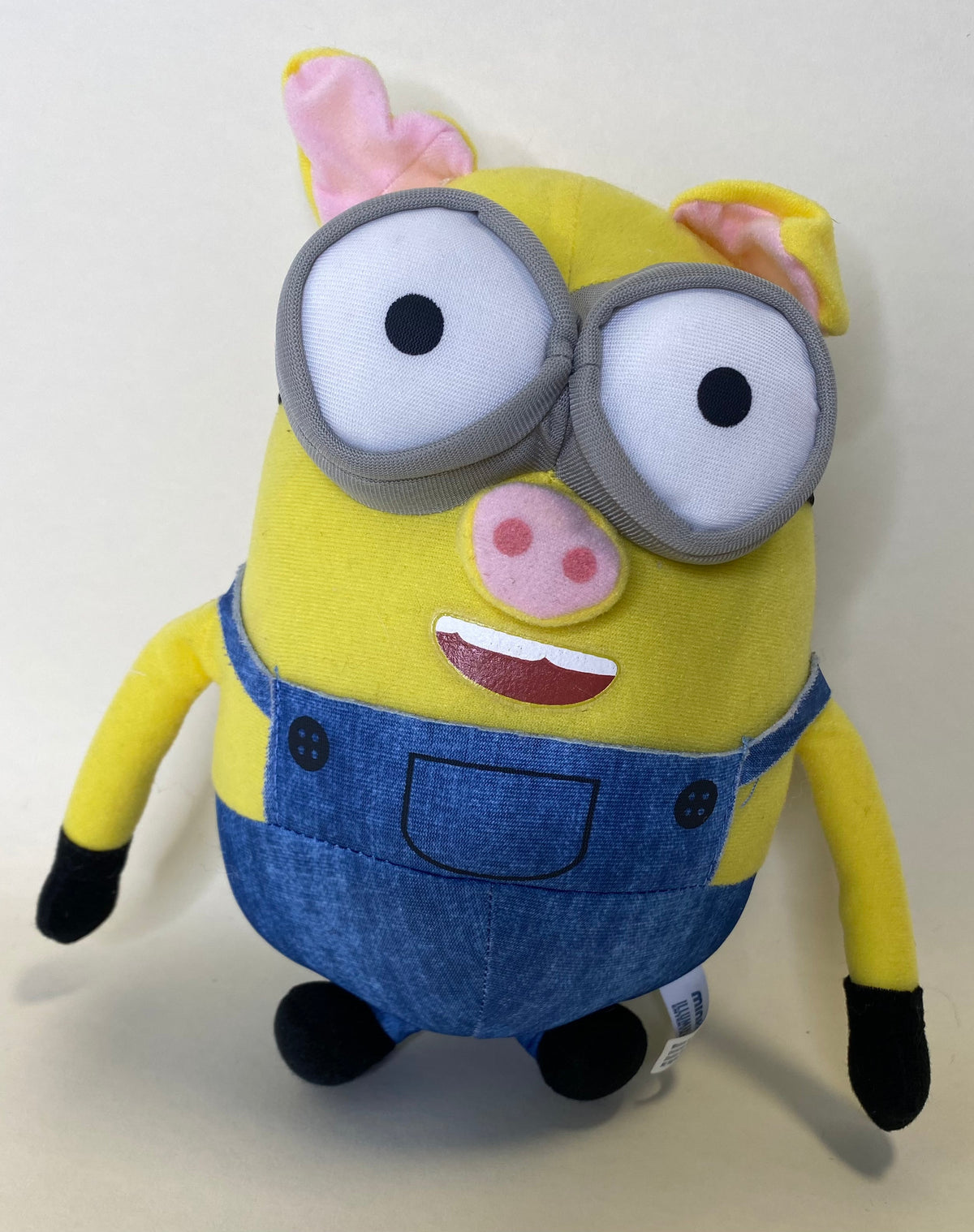 Yellow Minion plush with oversized gray goggles, blue overalls, and pink cheek patch