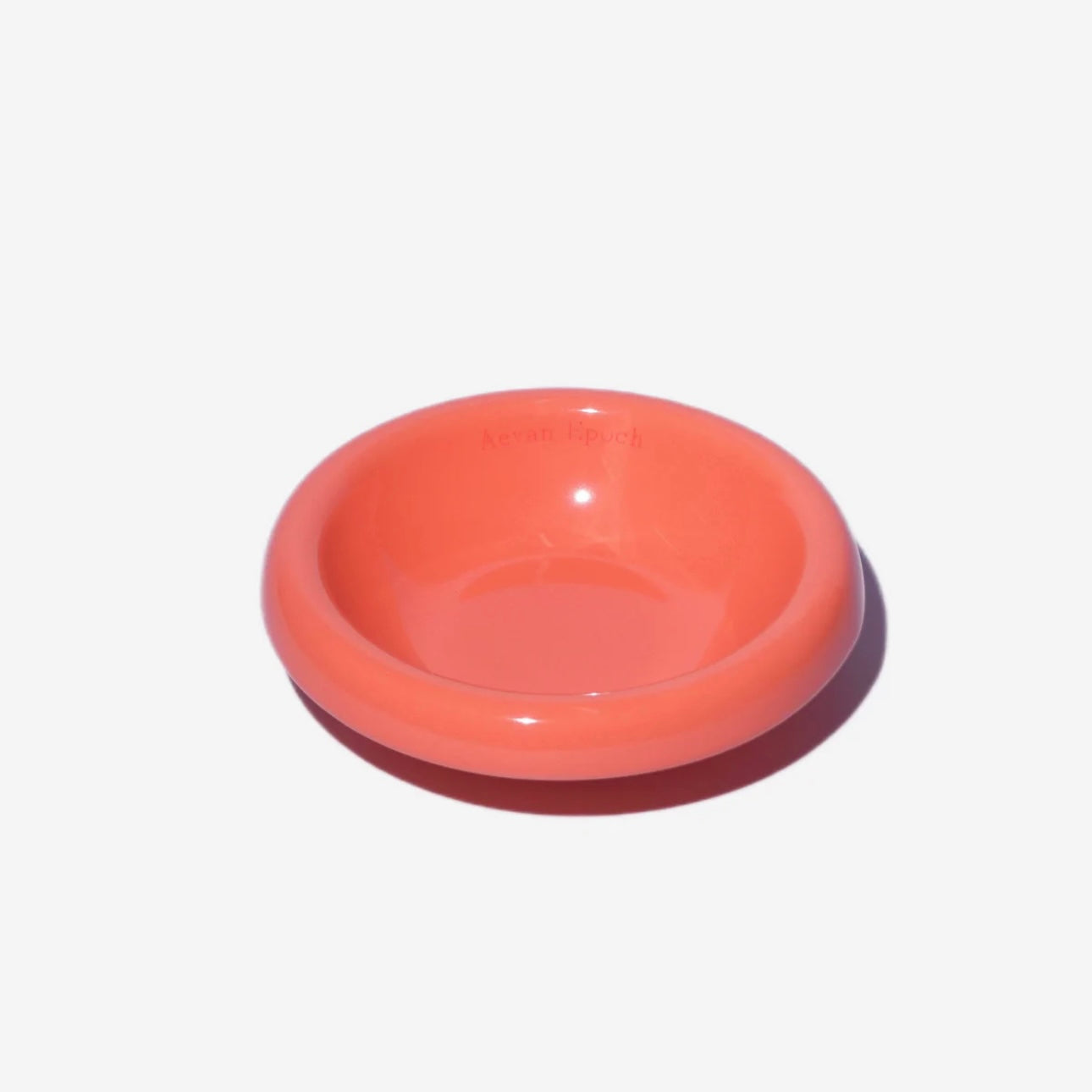 Stoneware pet bowl in coral red, round shallow dish with raised rim and glossy finish.