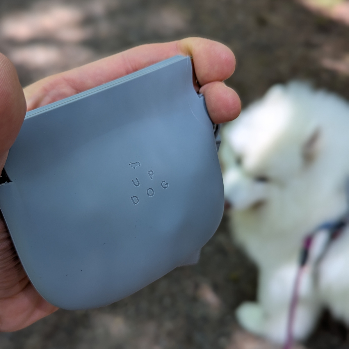 Blue-gray silicone treat pouch held in hand, with embossed brand mark and strap.