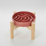 Pink/red wave slow feeder dog bowl on a wood stand with raised channels
