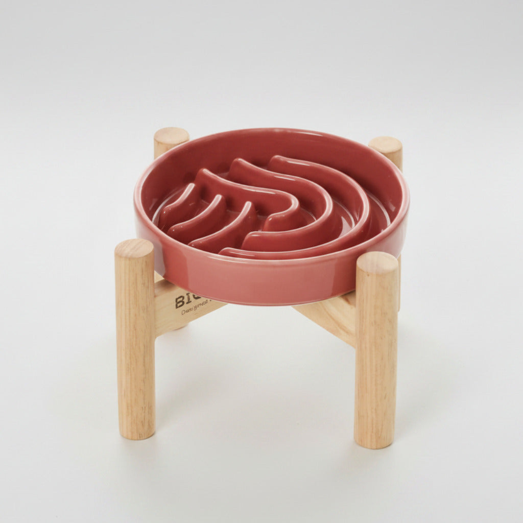 Pink/red wave slow feeder dog bowl on a wood stand with raised channels