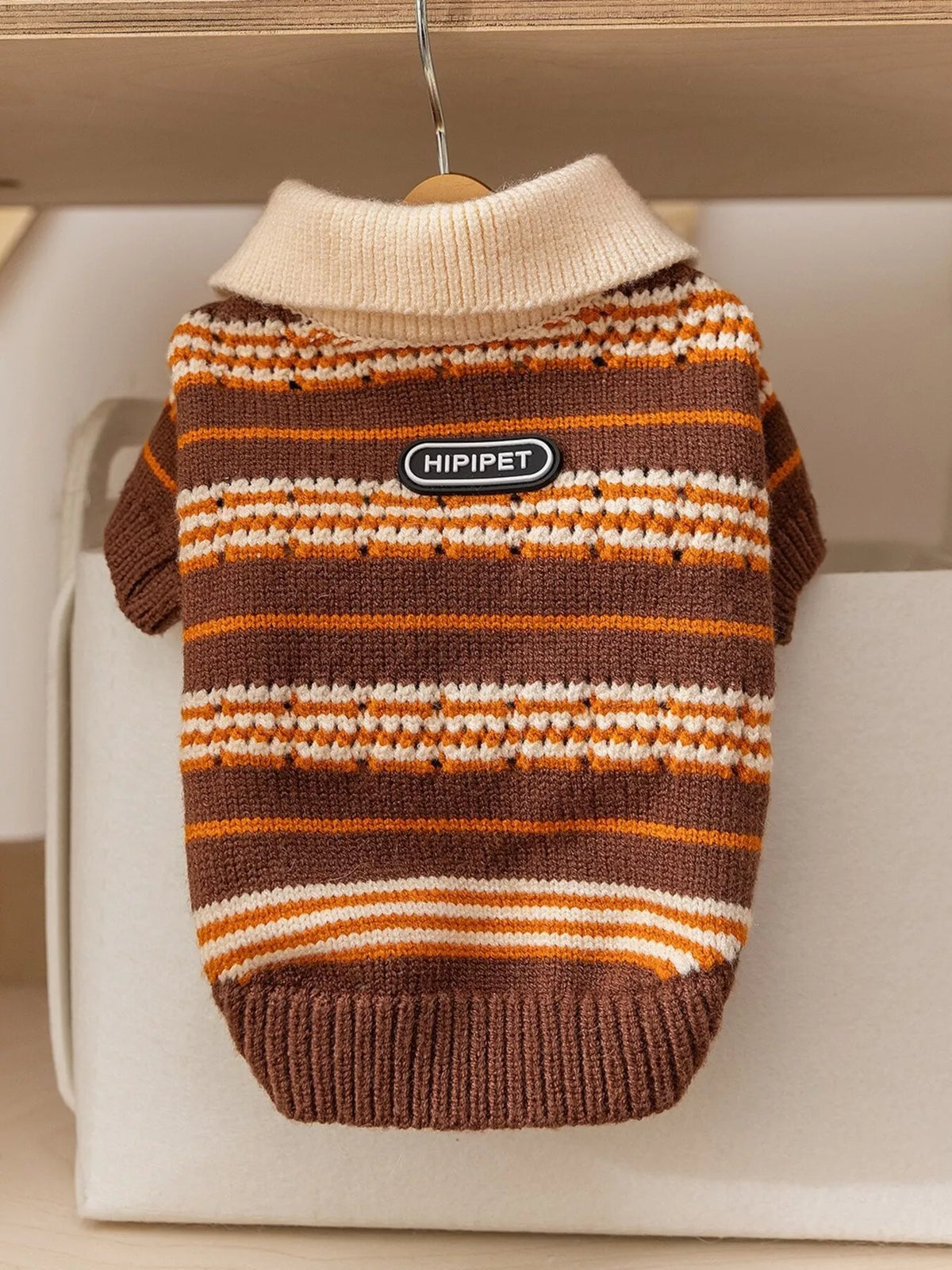 Brown knitted pet sweater with orange and white striped pattern and logo patch