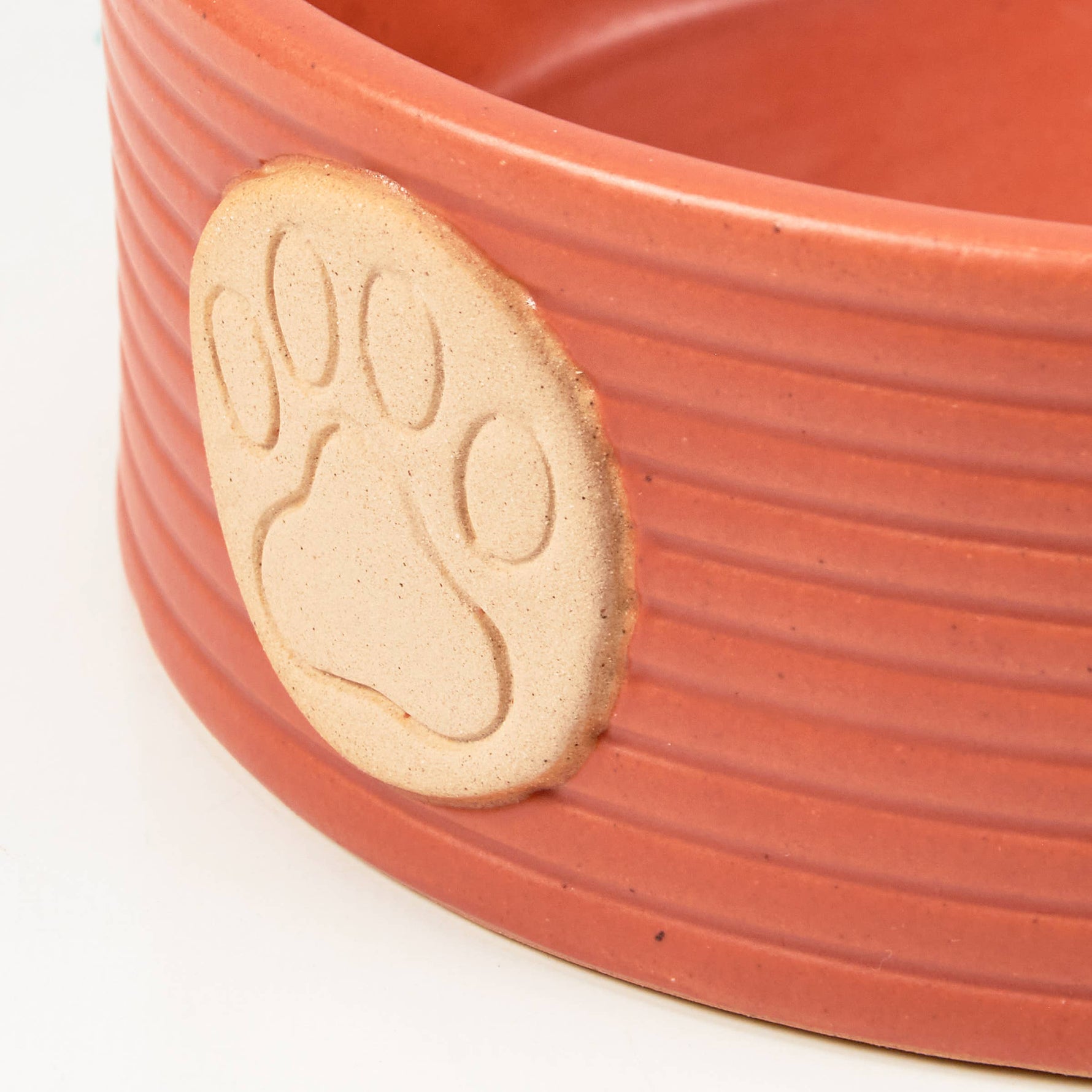 Orange pet bowl with close-up beige paw print on textured ribbed side
