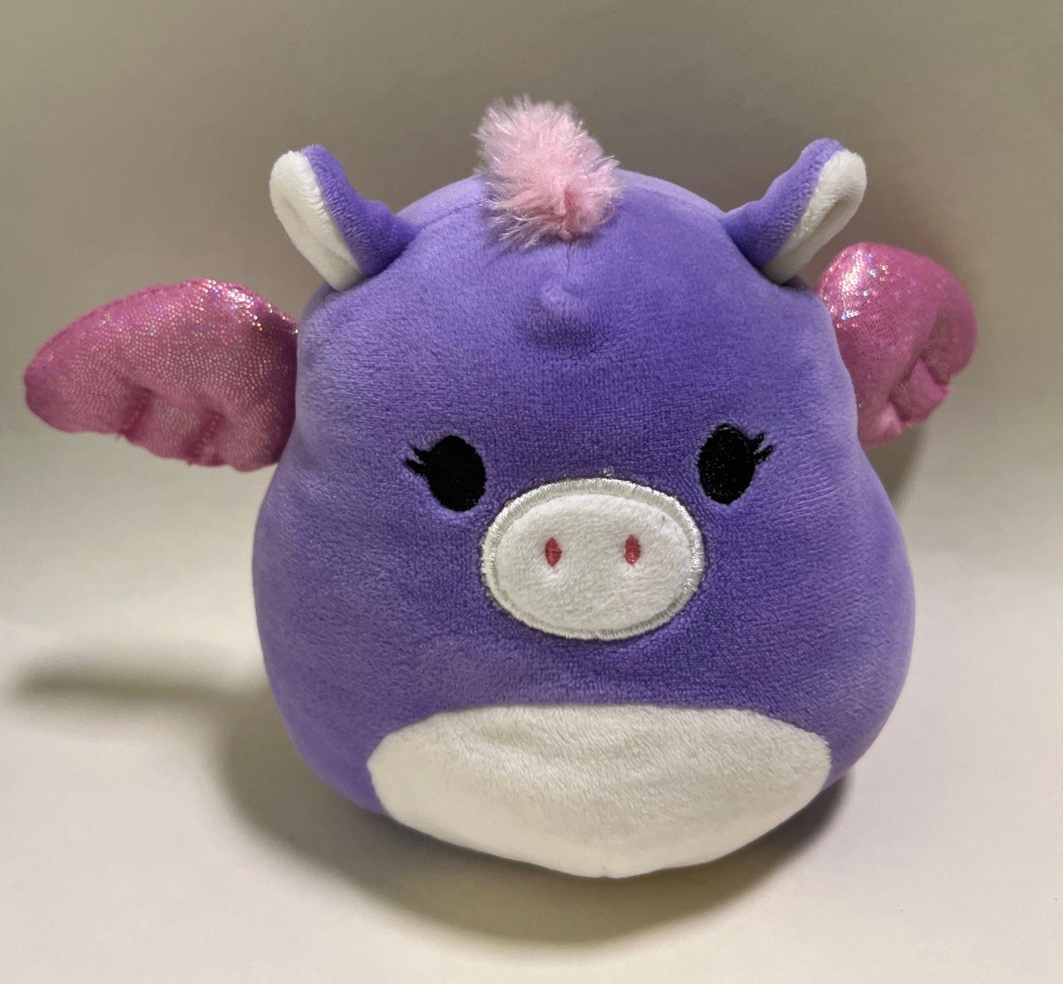 Large squishy plush pet toy, purple pig with pink ears, white muzzle, and pom-pom head.