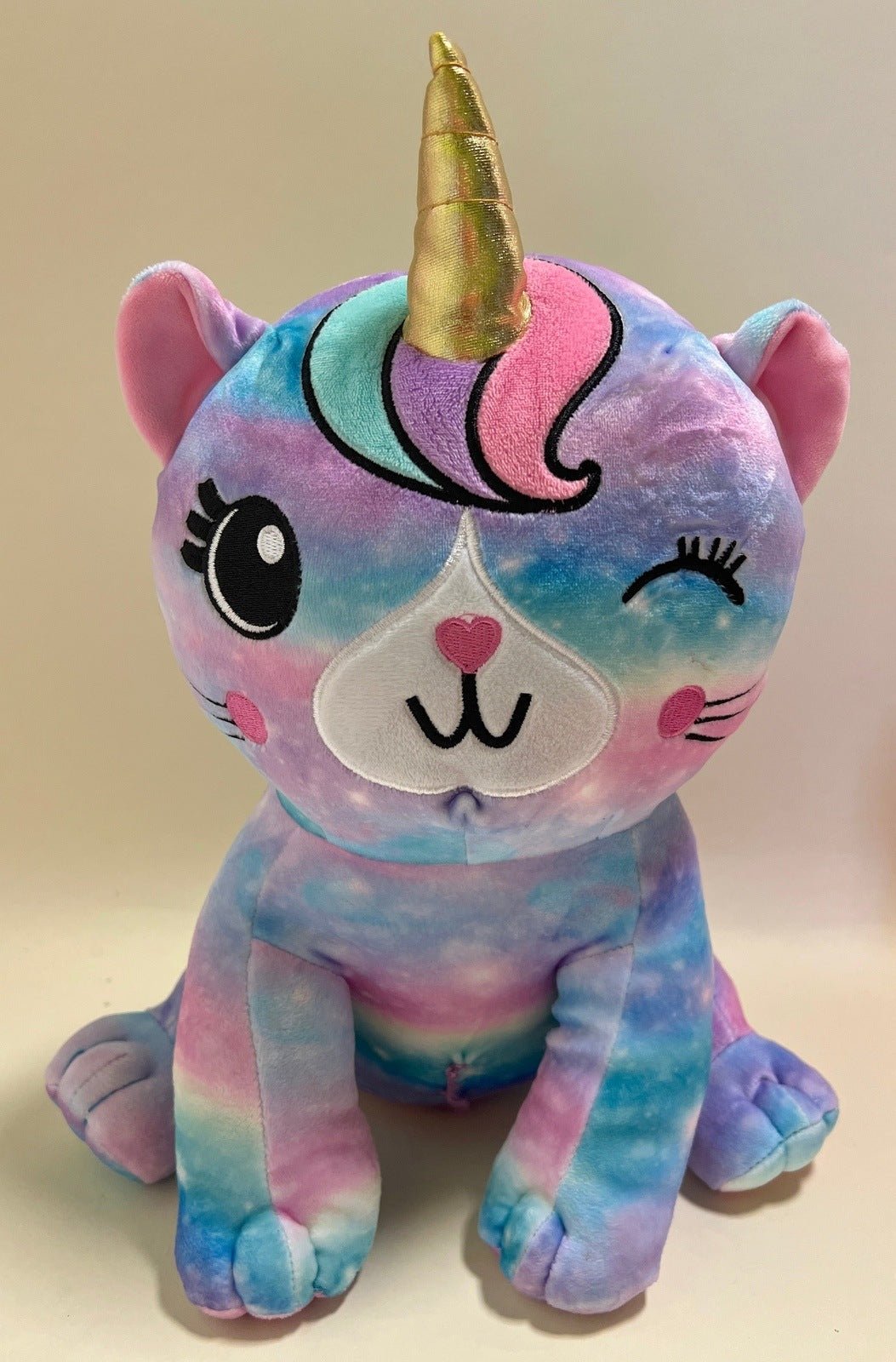 Large squishy plush pet toy, multicolor unicorn with gold horn and heart nose on face.