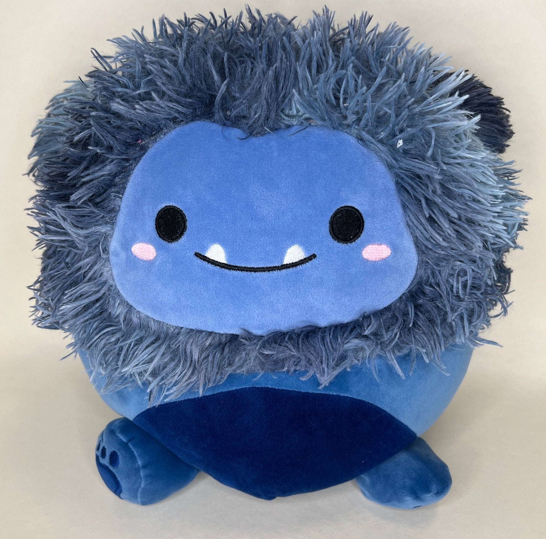 Blue shaggy plush cuddler with smiling face, rosy cheeks, and round body