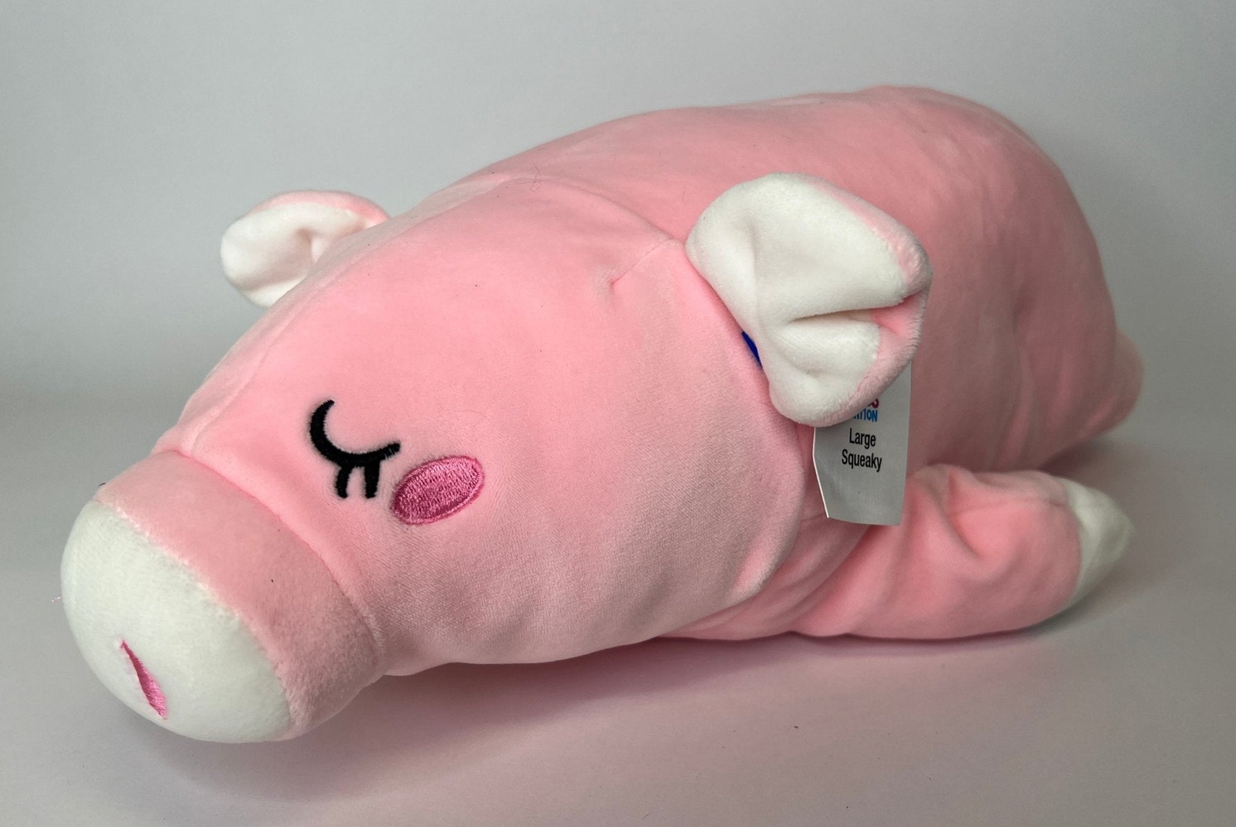 Pink plush pig cuddler with closed-eye smile, white paws, and soft rounded body