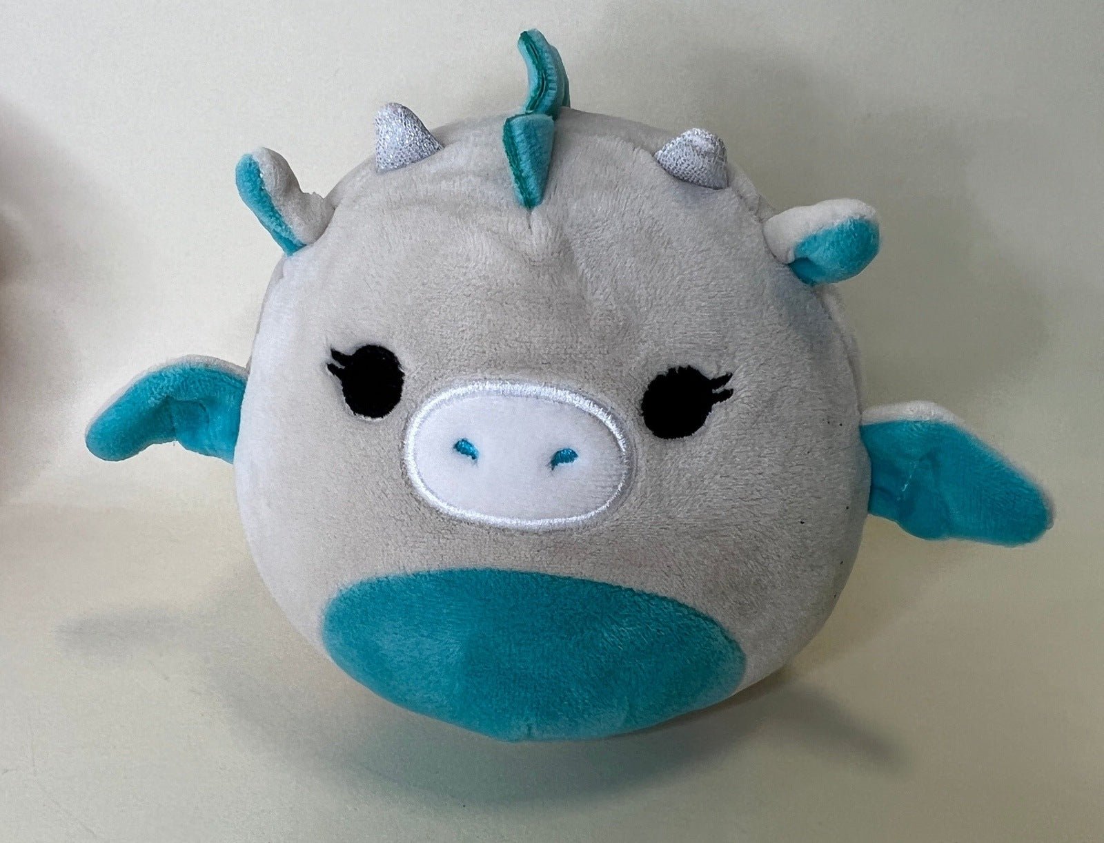Gray plush pet toy with teal horn accents, small wings, and smiling face