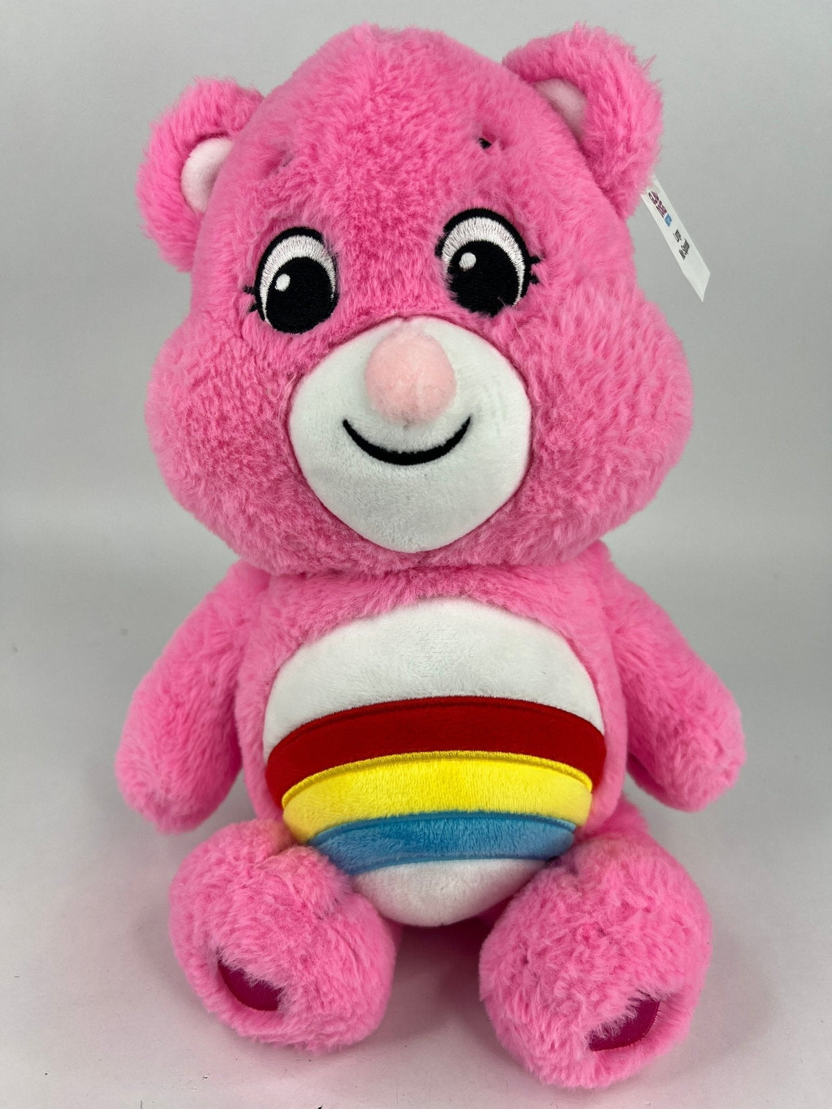 Pink plush dog toy bear with rainbow-striped belly patch and cute embroidered smile.