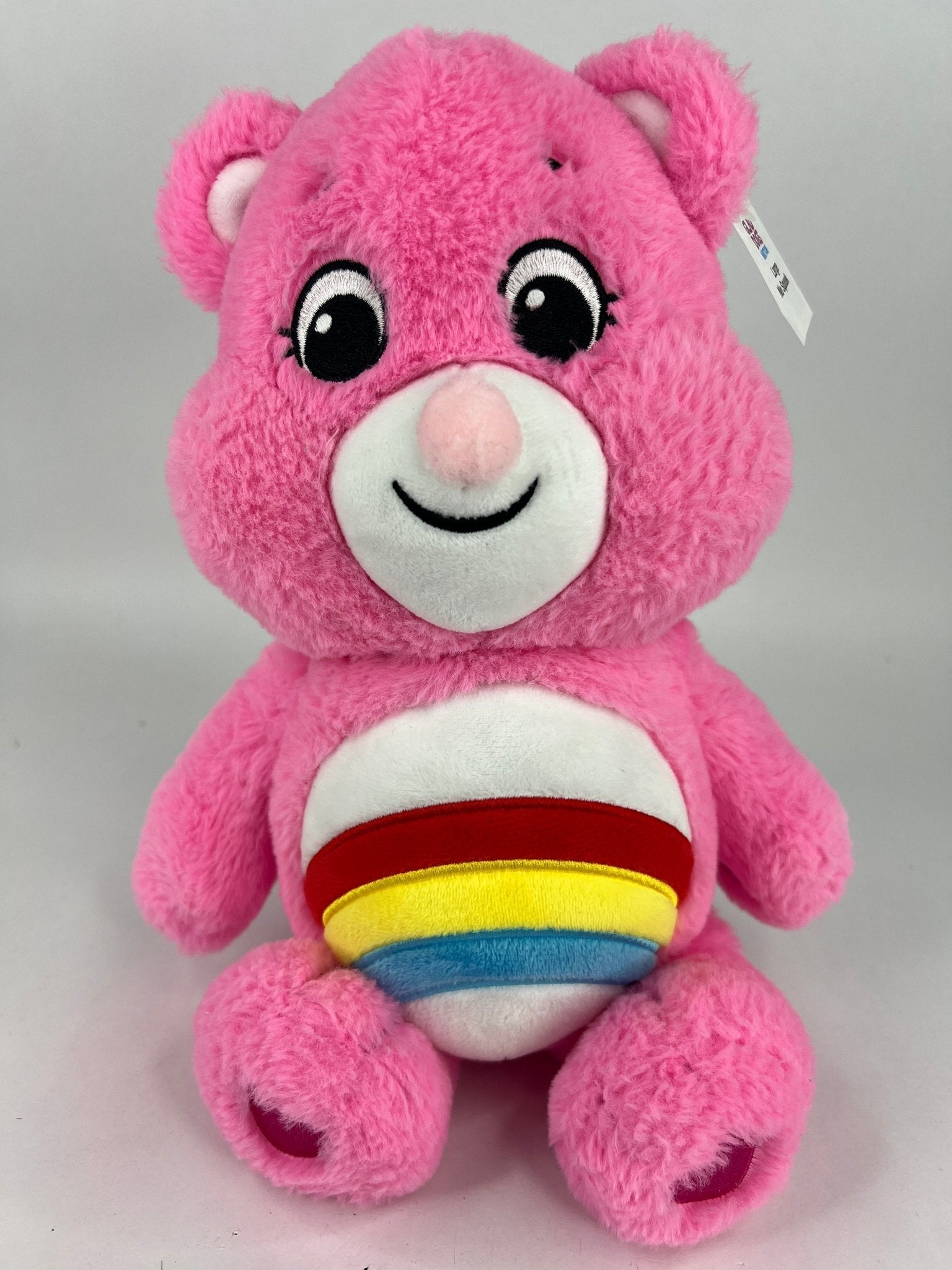 Pink plush dog toy bear with rainbow-striped belly patch and cute embroidered smile.