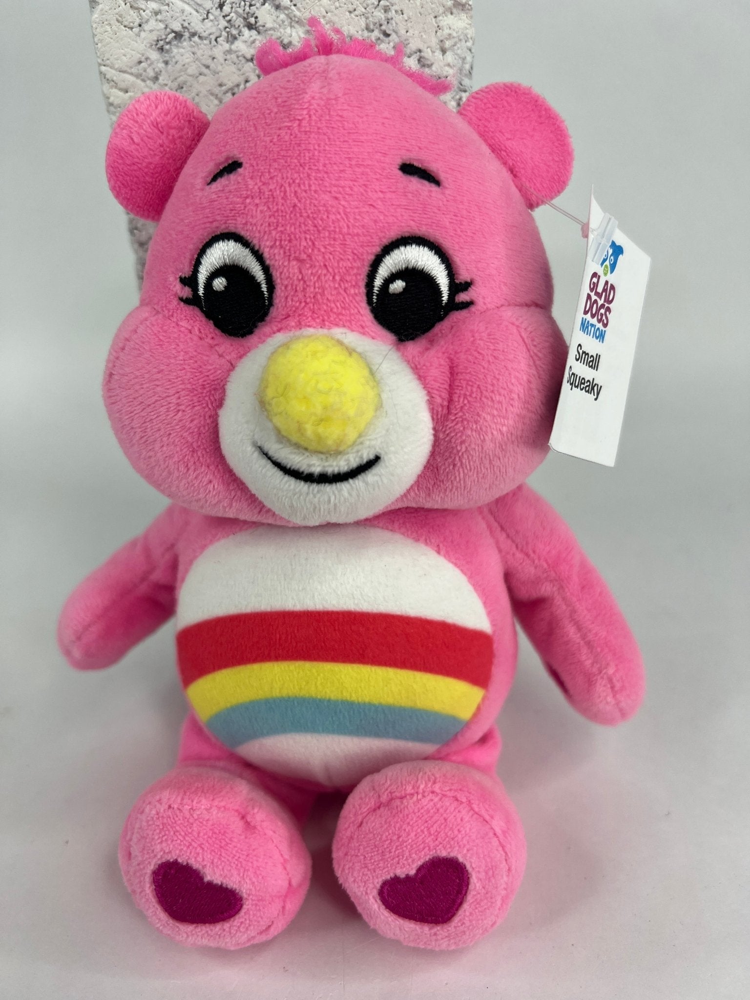 Pink plush dog toy bear with smiling face and rainbow belly print.