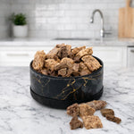 Black ceramic pet bowl with gold marble swirl, filled with dry kibble pieces