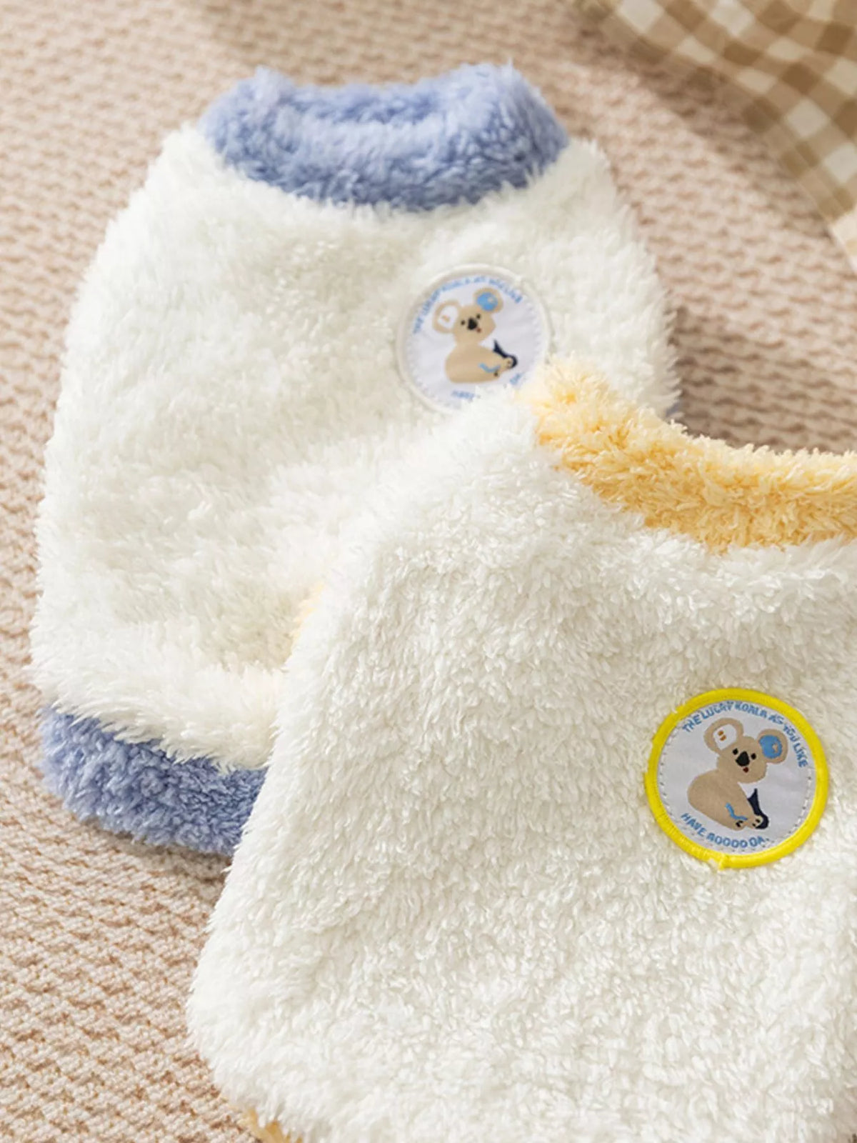 White plush pet sweater with light-blue trim and two round bear patch badges