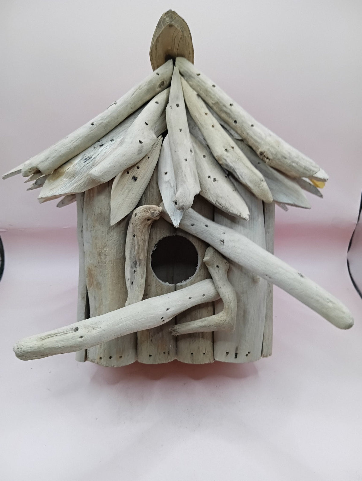 Driftwood birdhouse with round entrance hole and layered plank roof, weathered light wood