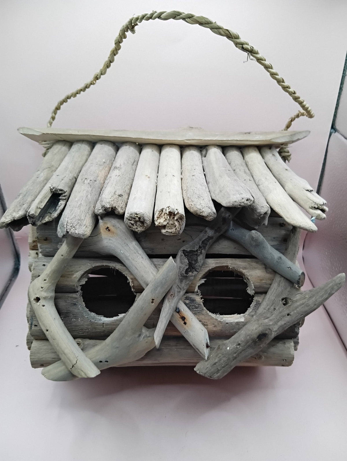 Weathered driftwood birdhouse with two circular entrance openings under slatted roof