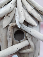 Close-up of weathered driftwood birdhouse with round entrance opening and curved perch
