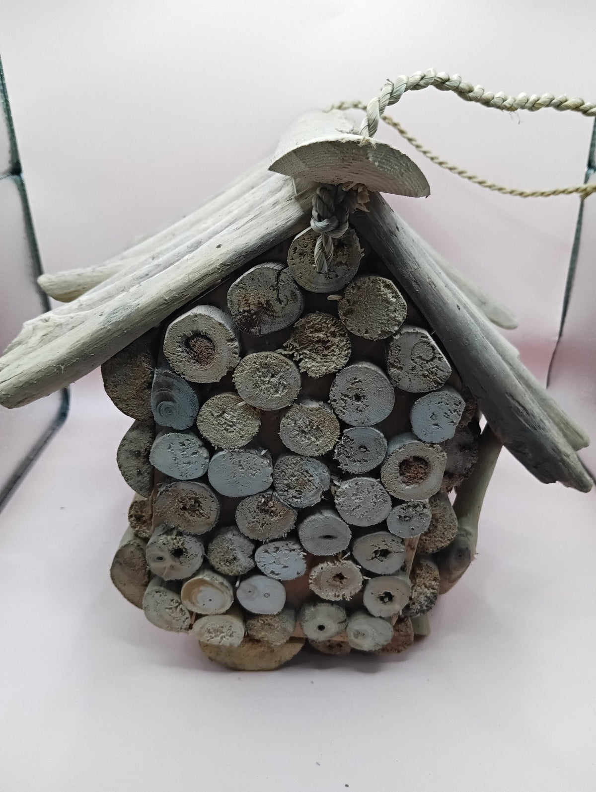 Driftwood birdhouse with open top, showing stacked firewood-style interior filler