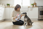 Blue packaged dog treat bag held near small dog sitting beside handler