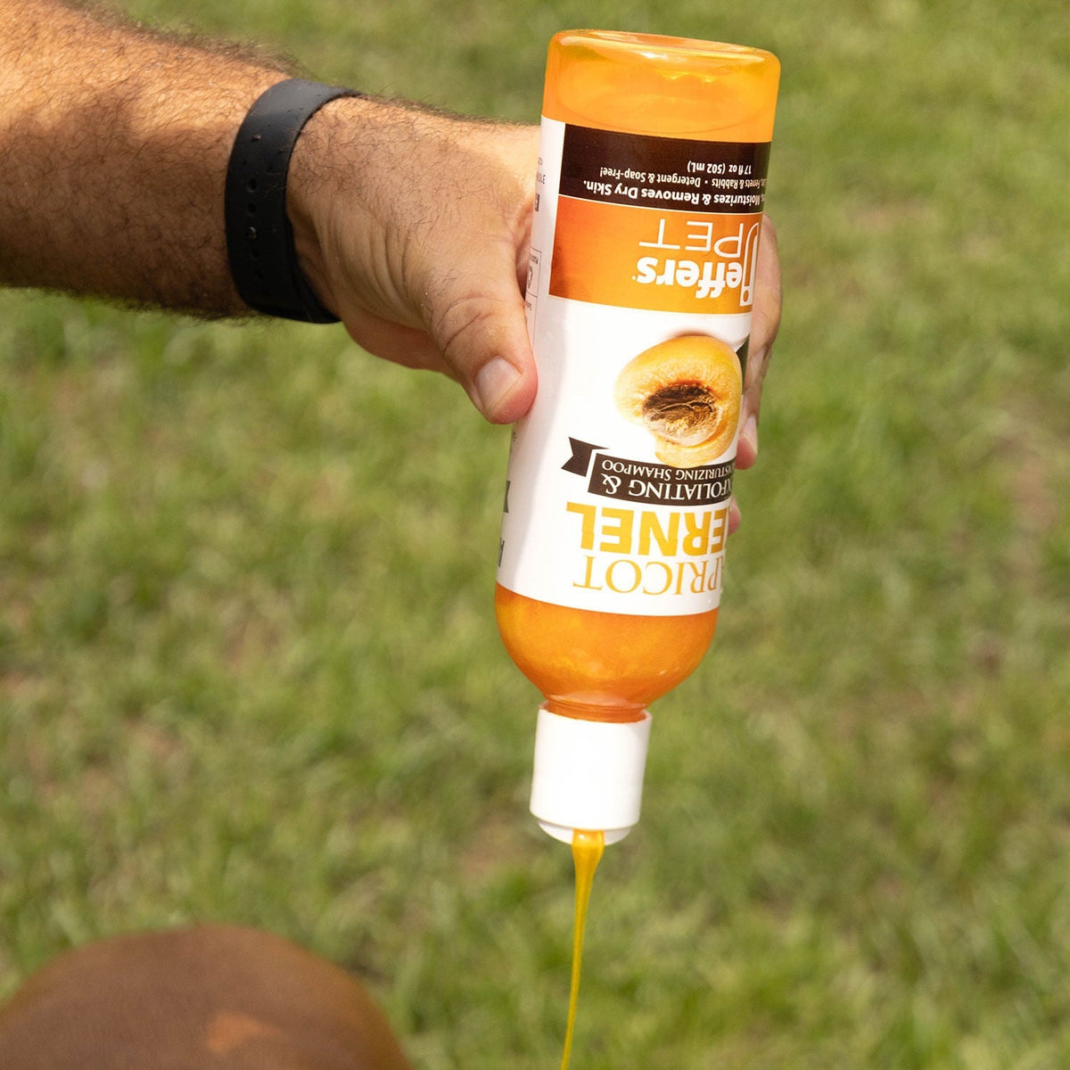 Apricot Kernel pet shampoo bottle in orange held in hand; yellow liquid drips from nozzle.