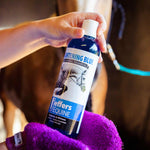 Hand holding blue-cap whitening horse shampoo bottle over purple grooming towel