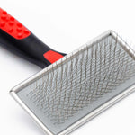 Pet slicker brush close-up: metal pin pad with black handle and red accents