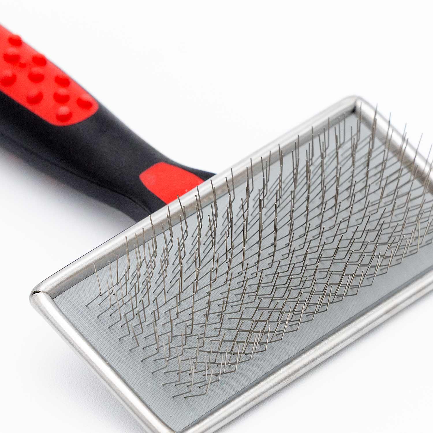 Pet slicker brush close-up: metal pin pad with black handle and red accents