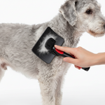 Self-cleaning slicker grooming brush with black base and red handle, brushing gray fur