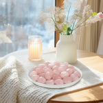 Rose quartz tumbled stones on a white plate, pale pink polished pebbles