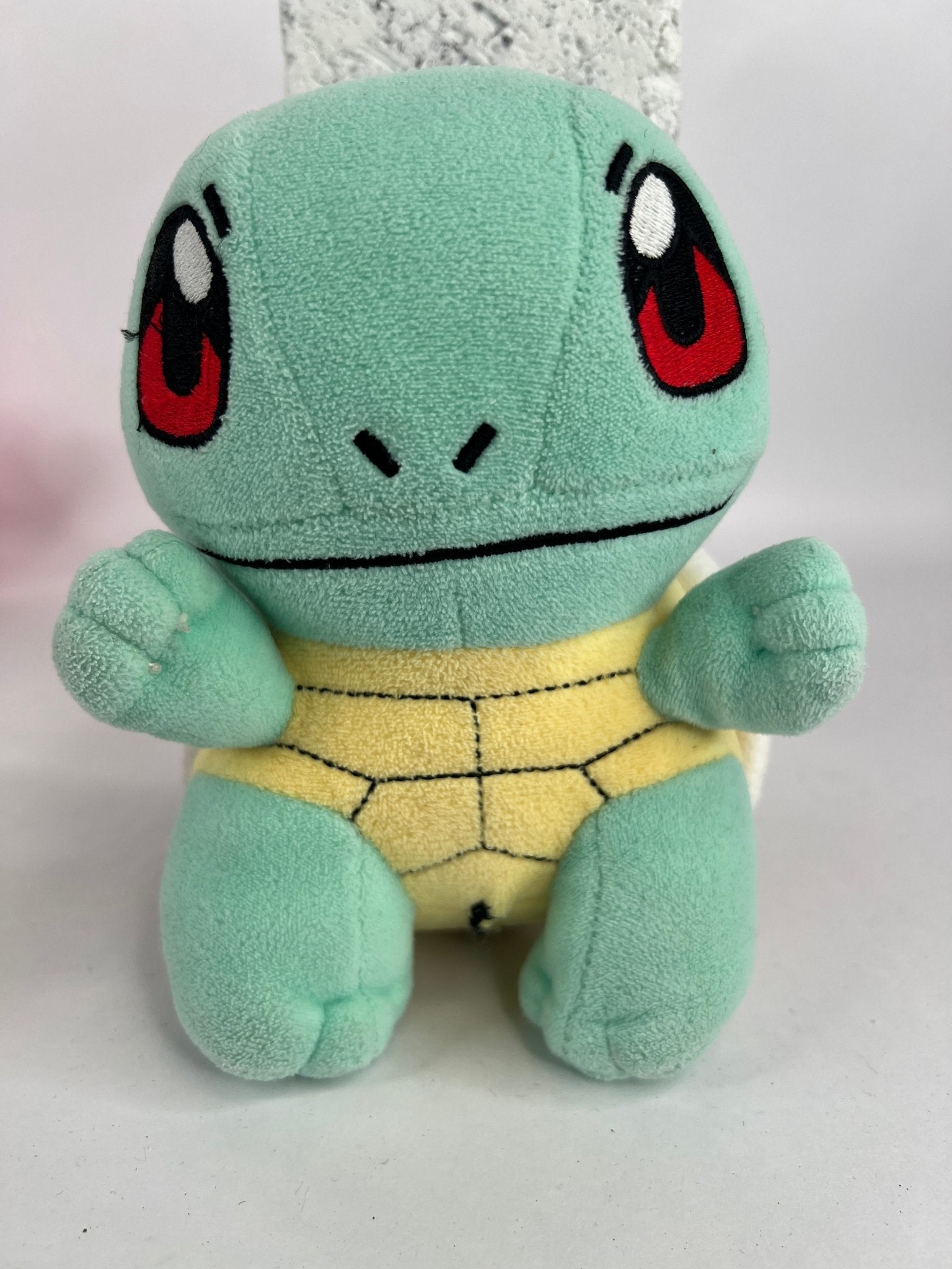 Stuffed plush dog toy, mint green cat-like character with black-red face markings and stitched smile