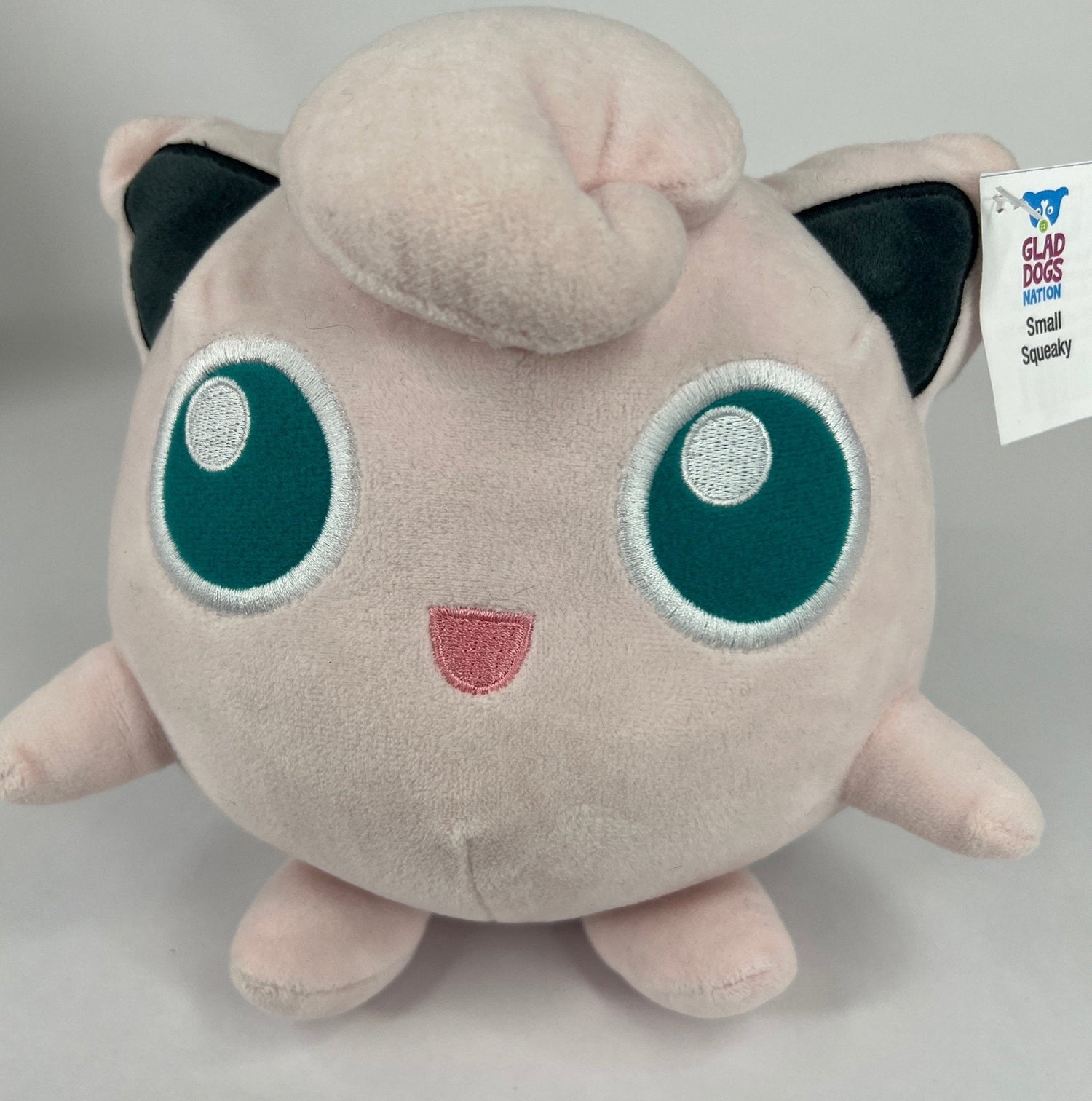 Stuffed plush dog toy, pale pink cat-like character with big teal eyes and squeaker tag