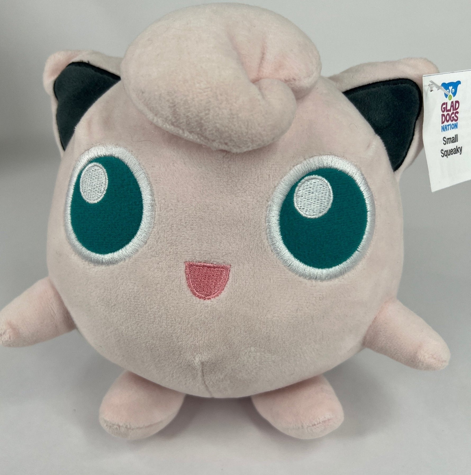 Stuffed plush dog toy, pale pink cat-like character with big teal eyes and squeaker tag