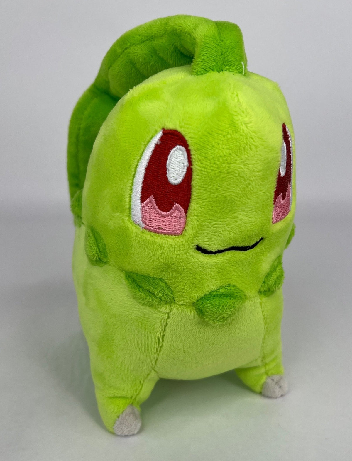 Green plush squeaky dog toy with cartoon face, rounded body and feet