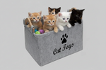 Light grey felt storage basket with paw-print logo and handles, holding cat toys