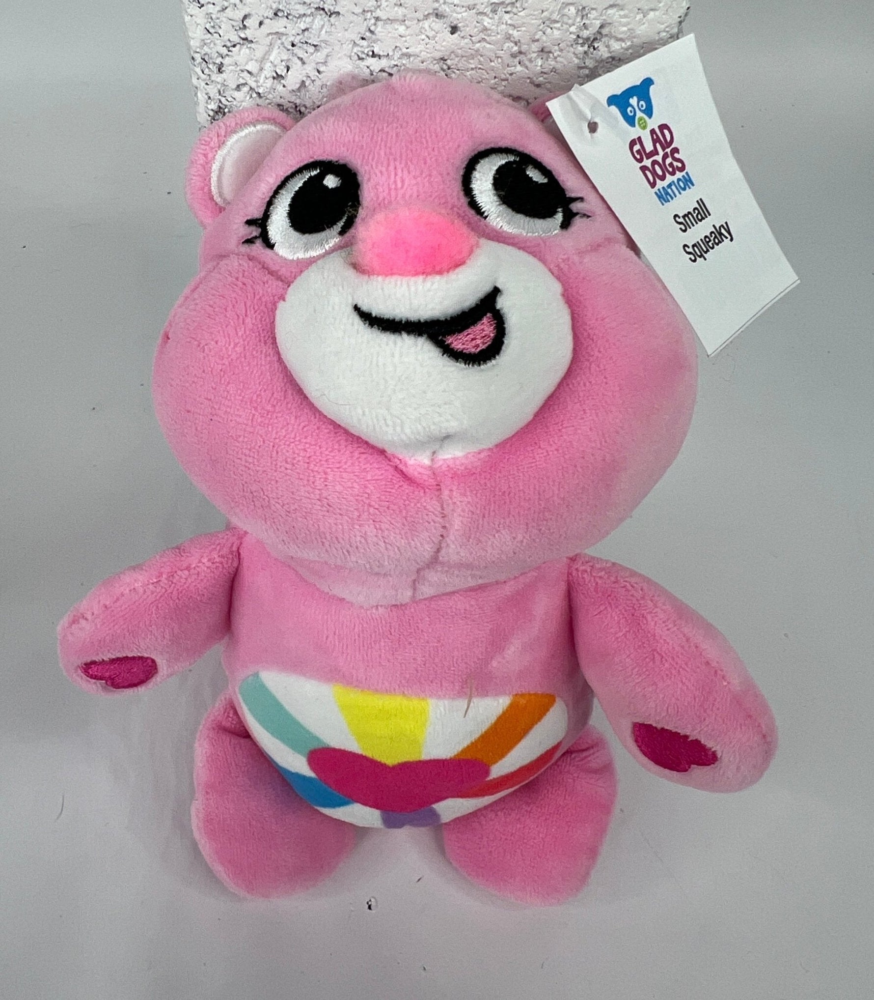 Pink plush dog toy bear with big eyes and rainbow belly graphic, stitched smile.